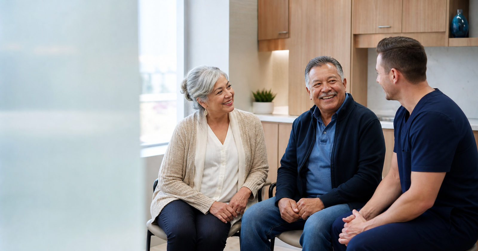 A denturist speaking with a smiling older couple in a bright consultation room